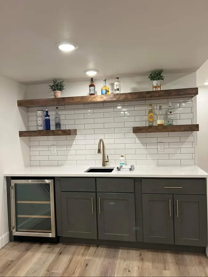 Basement wet bar with dark cabinets, white countertop, subway tile, and floating shelves