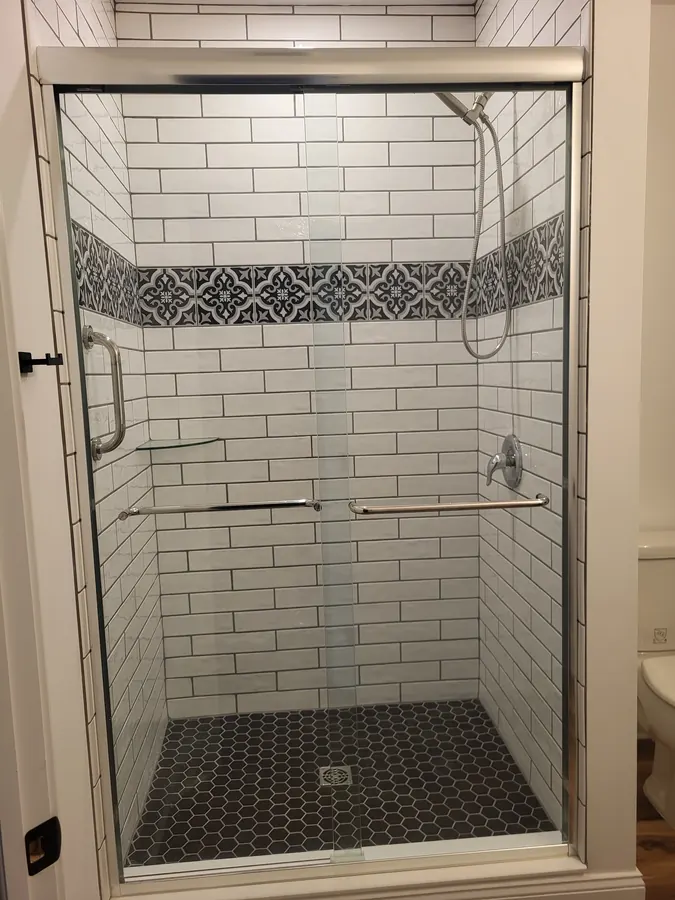 Basement bathroom shower with subway tile, patterned accent strip, and glass doors