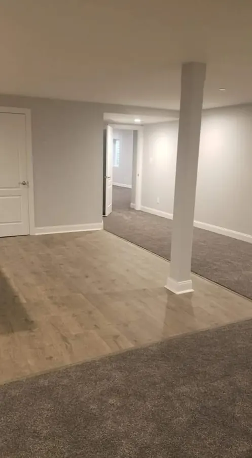 Finished basement with carpet and hard flooring zones divided by a support column